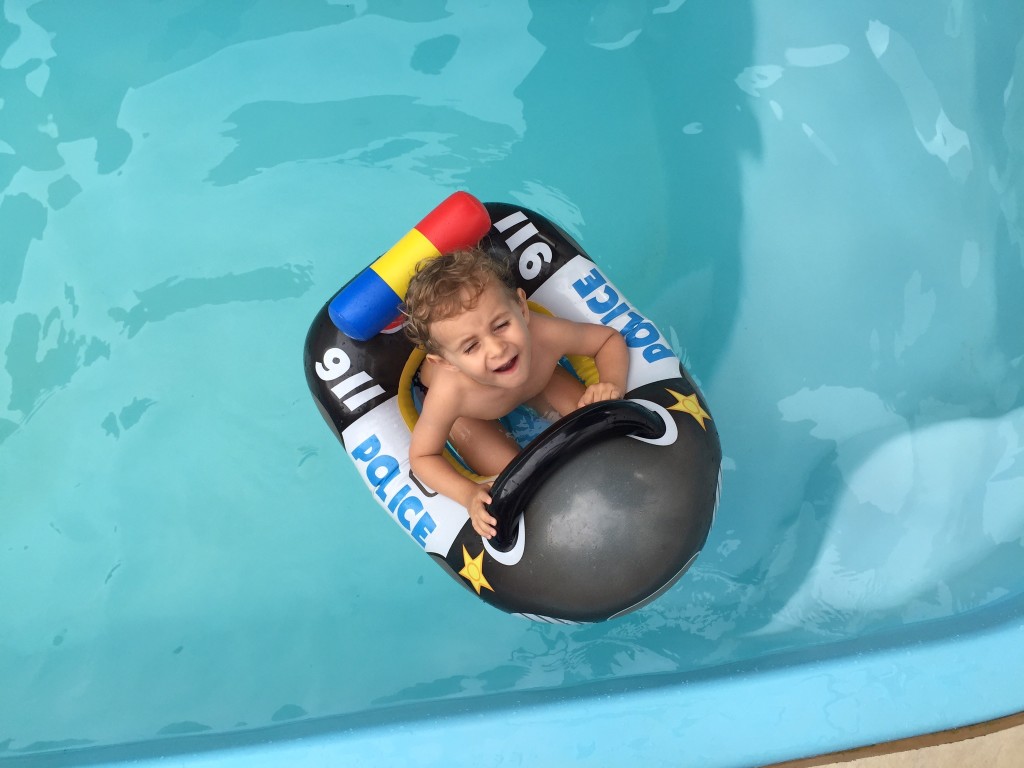 Menino pequeno brincando feliz na piscina durante as férias, aproveitando o tempo ao ar livre em um ambiente espaçoso.