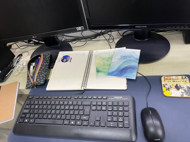 Planner 2026 personalizado aberto sobre a mesa de trabalho, com canetas e materiais de scrap ao redor.